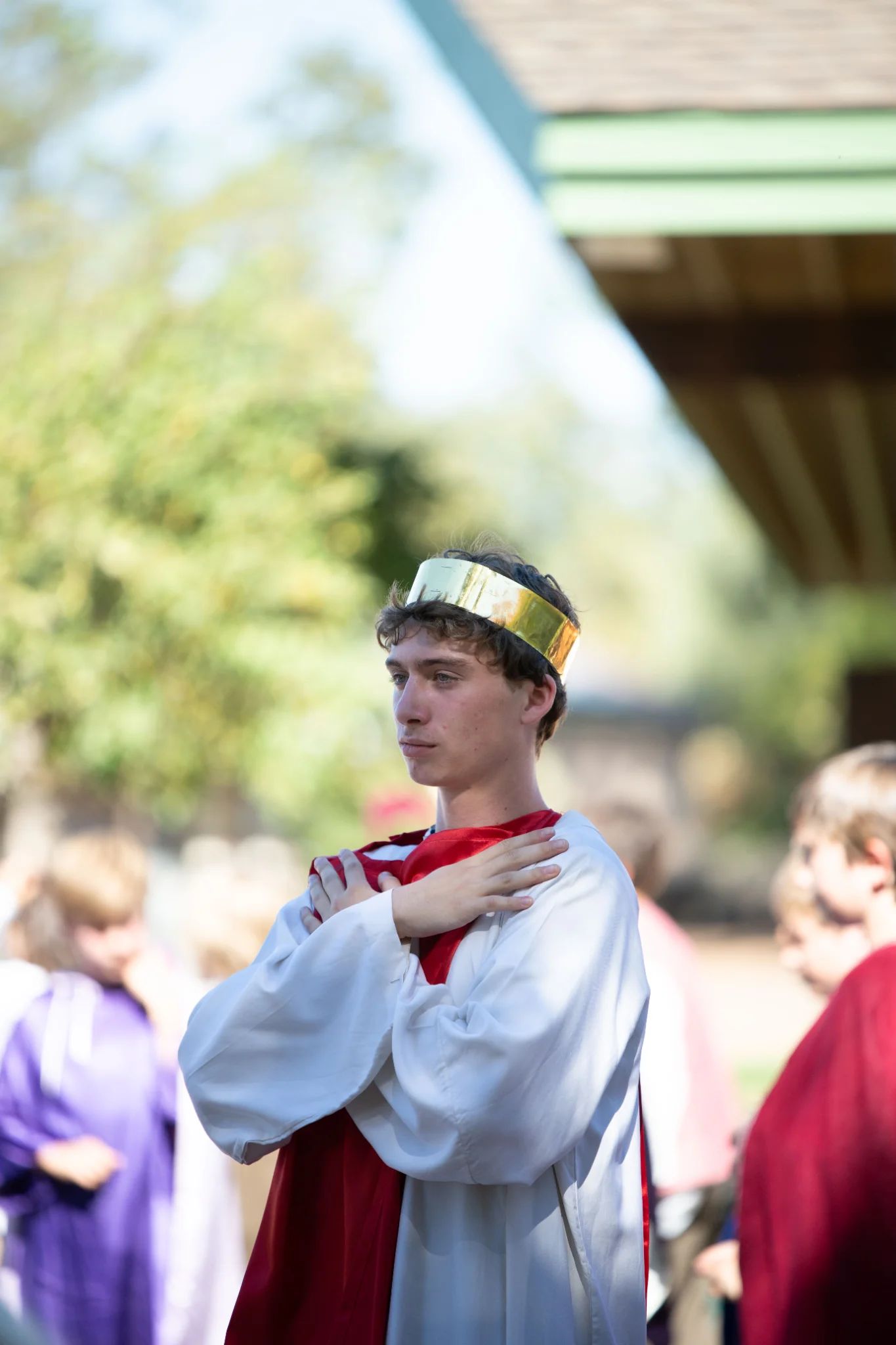High school student in white tunic with red and gold crown stands with hands crossed over chest