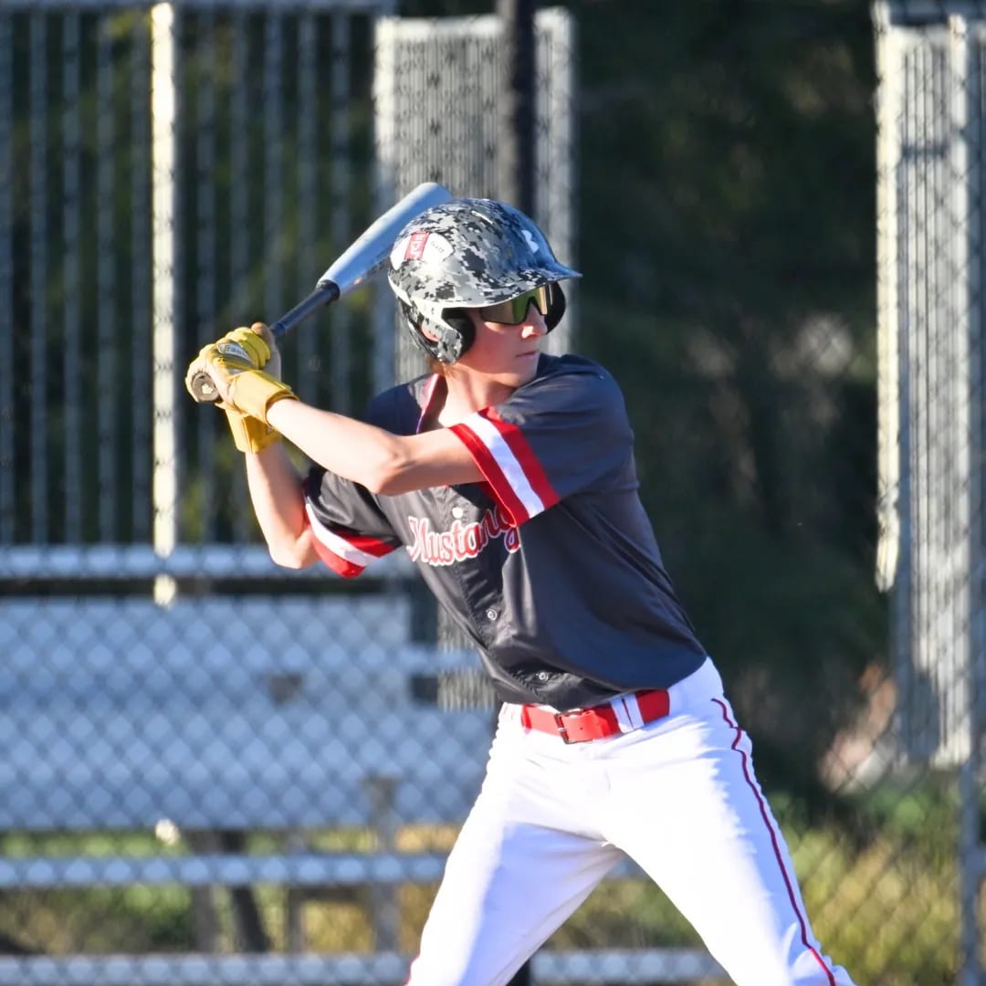 A Mustangs batter waits on the pitch in evening light.