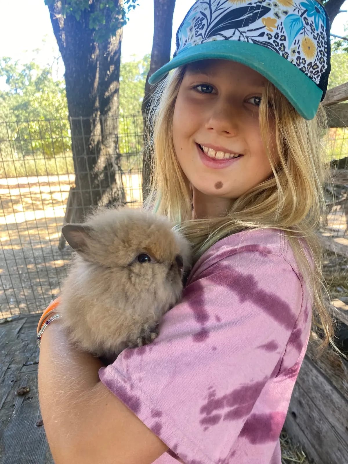 A camper in a sun hat smiles while holding a fluffy lionhead bunny at the farm's animal pens