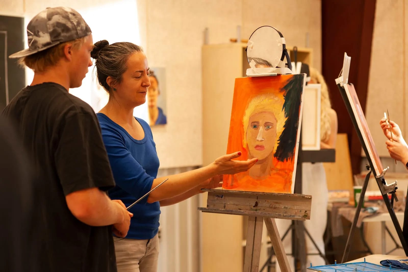 Angie Brown, Practical Arts Teacher at Summerfield Waldorf School & Farm, offering instruction on a G12 student's self-portrait artwork.